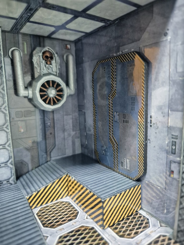 A futuristic interior scene featuring dark walls with industrial designs, including a skull emblem, pipes, and a heavy-duty door marked with warning stripes.