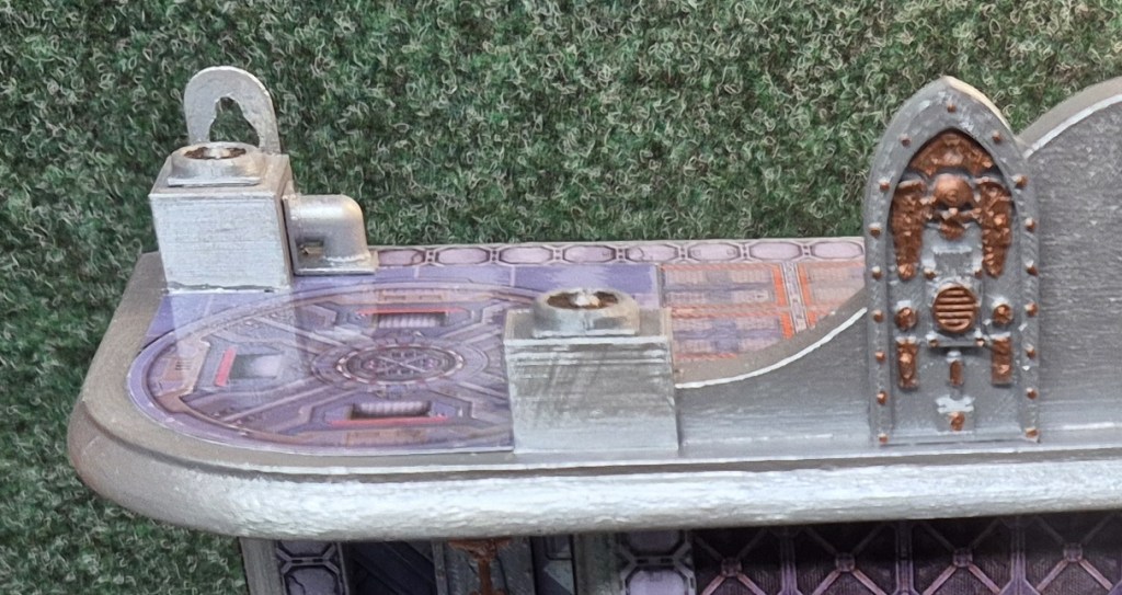 A detailed close-up of a model's rooftop featuring various textures, metallic elements, and a purple patterned surface, set against a green backdrop.